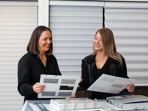 Two women sitting at a desk looking at fabric samples